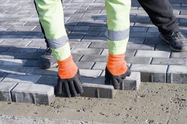 Concrete contractor placing brick pavers by hand for residential driveway installation in Medina, OH