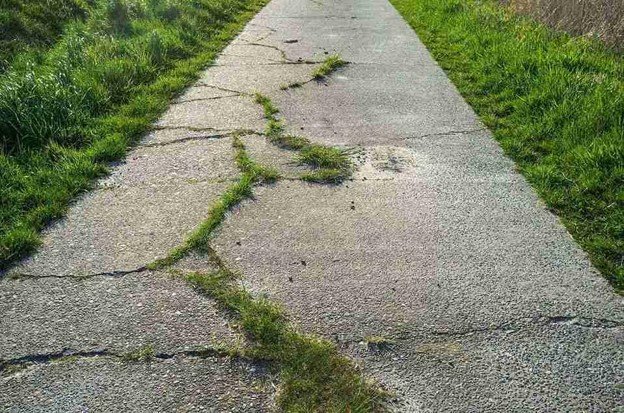 Cracked and damaged concrete driveway with visible wear and weeds growing through the surface in Middleburg Heights, OH
